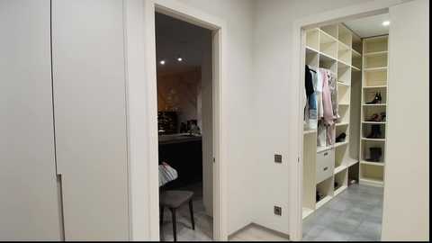 Video of a modern, minimalist bedroom with white walls, a walk-in closet on the right, and a partially open door leading to a study area with a desk and chair.