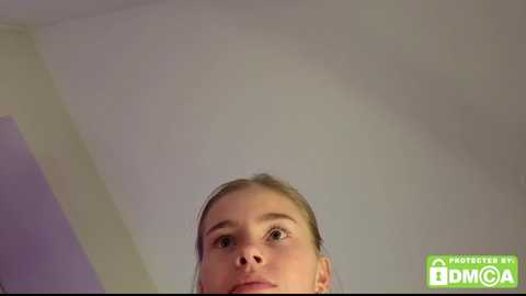 A video of a young woman with light skin and brown hair, captured from a low angle, gazing upward. The background is a plain, light-colored ceiling. A green text box reads \"NASTYFILTHY BY DMMCA.\