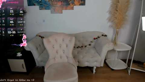 A video of a plush, cream-colored tufted armchair with a white cushion and a decorative garland, set against a white wall with colorful abstract art.