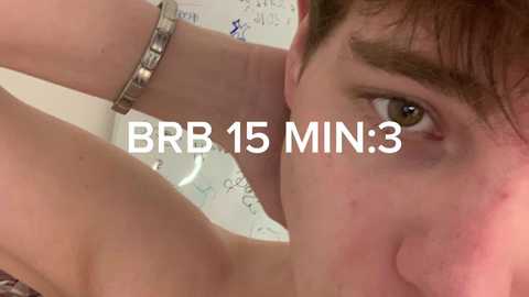 A close-up video of a young man with short brown hair, light skin, and a silver bracelet, looking intensely at the camera. Text overlay reads \"BB 15 MIN:3\". Background is blurred.