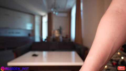 Video of a blurred indoor room with a white table, a blurry person's leg, and a Christmas tree in the background.