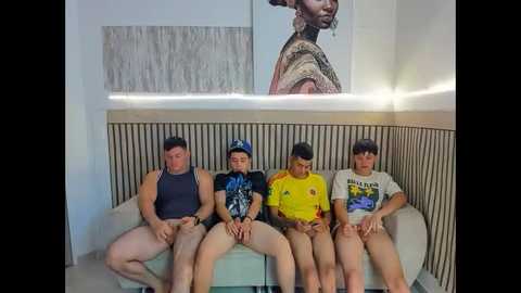 Video of four teenage boys, sitting on a beige couch, wearing casual T-shirts and shorts, in a modern, minimalist room with a large abstract painting and vertical wooden paneling.