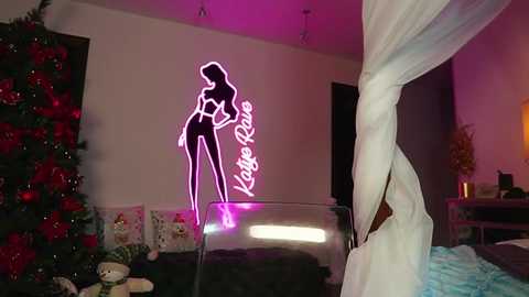Video of a modern bedroom with a neon \"Katy Perry\" sign on the wall, a Christmas tree adorned with red ornaments, and a white canopy bed.