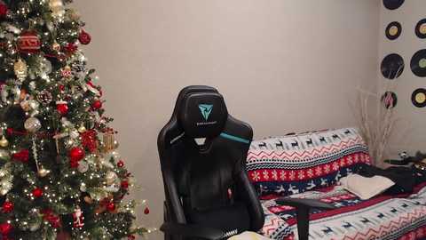 Video of a black gaming chair with a blue triangle logo in a festive room. Christmas tree adorned with red and gold decorations on the left, a couch with a red and white patterned blanket on the right.