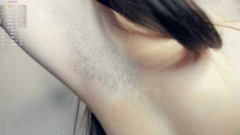 Close-up video of a woman's upper body, showing her armpit hair and the beginning of her dark brown hair. The skin is pale, and the background is blurred.