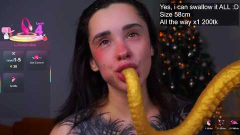 Video of a young woman with long dark hair, wearing a dark patterned top, seductively eating a large yellow banana in front of a Christmas tree. Text overlay includes a Twitch chat message.