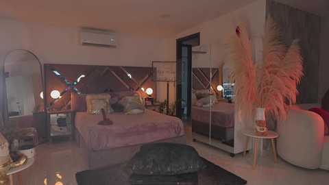 Video of a modern, cozy bedroom with a large bed, mirrored headboard, pink bedding, and decorative plants.