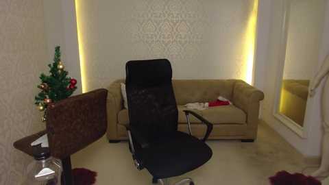 Video of a modern, minimalist living room with beige walls, a cream sofa, a black office chair, a small Christmas tree, and decorative lighting.