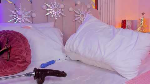 Video of a cozy bedroom with a white bed, plush pillows, and a plush red pillow. Silver star-shaped wall decor, a screwdriver, and a dark dildo on the bedspread.