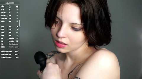 A video of a pale-skinned woman with short dark hair, wearing a strapless top, holding a black makeup brush, focused on her reflection in a mirror, with a digital overlay displaying makeup instructions.