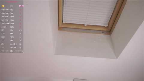 Video of a ceiling with a small, square skylight, partially covered by white blinds, above a white wall. A digital calendar with pink and purple accents is displayed on the left.