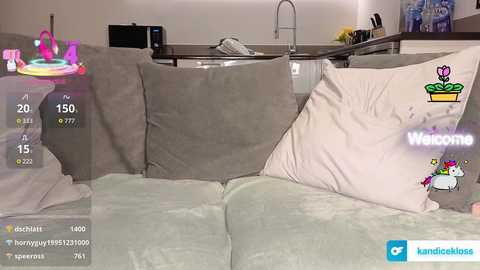 Video of a modern living room with a beige sofa, a glass coffee table, and a kitchen area visible in the background. The image includes a digital overlay with social media icons and a \"Welcome\" message.