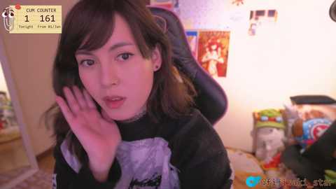 A young woman with long brown hair, wearing a maid outfit, poses in a dimly lit room, with posters and snacks in the background.