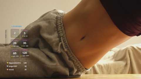 Media: Video of a person's midsection in loose gray sweatpants, with a digital fitness tracker overlay showing steps and heart rate. Background shows a bed with a beige blanket.