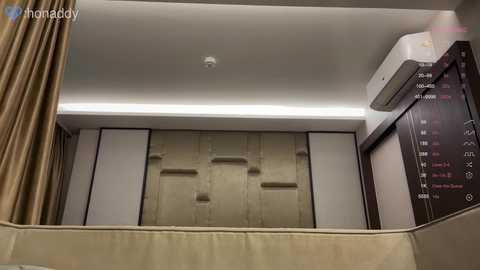 Video of a modern, minimalistic room with beige wall panels, an air conditioning unit, and a beige curtain. The room features a simple, clean design with a large clock on the wall.