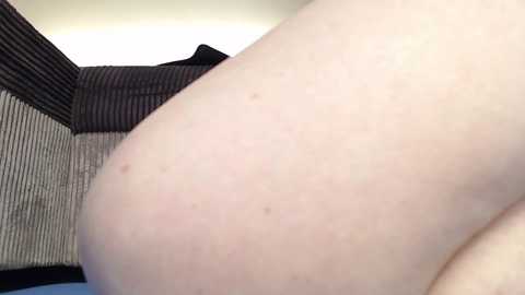 Media: Video of a pale-skinned person's bare buttocks with a few small blemishes, lying on a striped, textured surface. The background shows a black and white patterned cushion.