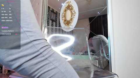 A video of a person wearing light gray pants, standing in front of a glass door with a decorative oval mirror, reflecting a room with a chandelier and bookshelves.