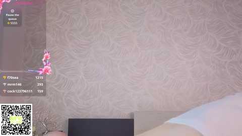 Media: Video of a bedroom wall with floral wallpaper and a QR code. The wallpaper has a subtle, swirling pattern. A smartphone screen displaying a social media post is partially visible on the left.