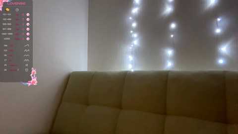 Media: A video of a dimly lit room featuring a beige tufted couch against a wall adorned with string lights. To the left, a colorful chart with various symbols is visible.