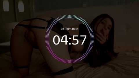 A dimly-lit video captures a woman in black lingerie, bent over a bed, with a \"Be Right Back\" overlay and a clock reading \"04:57.\