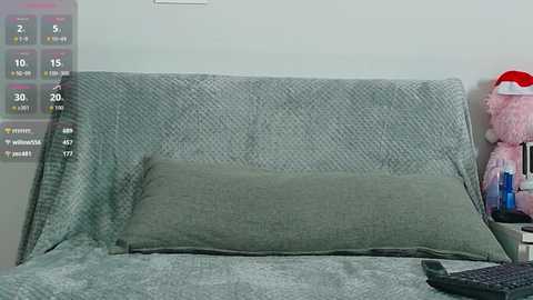 Video of a cozy bedroom with a grey, textured headboard, a green pillow, and a pink stuffed animal on a white nightstand, with a digital clock displaying 30 minutes.