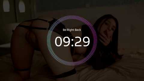 A dimly-lit video shows a woman in black lingerie and thigh-high stockings on all fours on a bed, with a digital clock overlay reading \"09:29\" and \"Be Right Back\" text.
