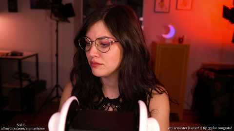 Video of a young woman with long black hair, wearing glasses and a black lace top, speaking into a microphone in a dimly lit room with a crescent moon nightlight.