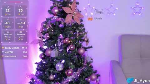 Video of a decorated Christmas tree with purple lights, gold ornaments, and a glittery star on a white wall. A digital screen shows weather data on the left.
