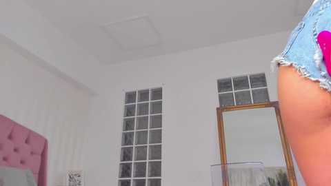 Media: A video of a woman's denim-clad bottom, seen from behind, in a modern, minimalist room with white walls, a glass-block window, and a mirror.