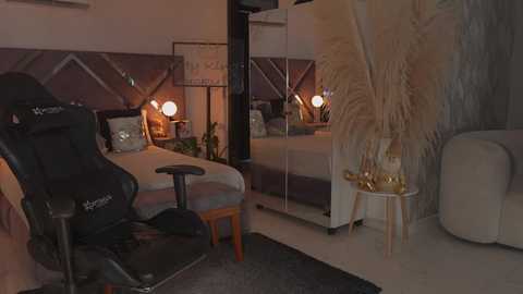 Video of a cozy, modern bedroom with a black gaming chair, a plush bed, warm lighting, a large mirror, and elegant decor.
