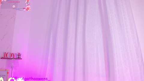 Video of a white curtain with soft folds, illuminated by pink and purple light. \"MOM\" and \"DAD\" letters on a shelf in the background.