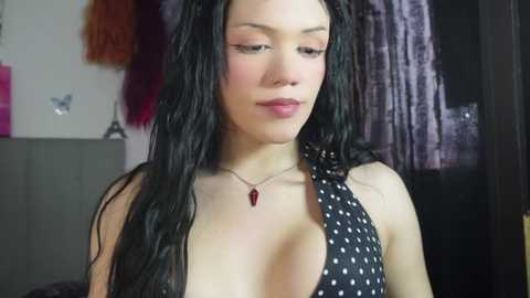Video of a young Asian woman with long, wet black hair, wearing a black halterneck dress with white polka dots, standing indoors by a window.