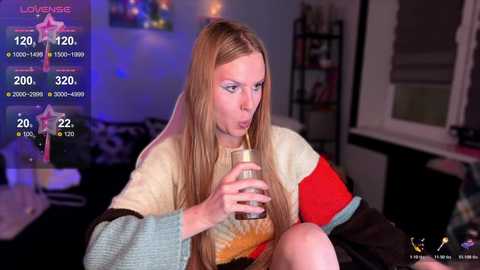 Video of a blonde woman in a cozy living room, drinking from a glass, wearing a multicolored sweater, with a \"Love Island\" overlay showing stats.