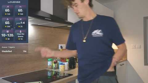 A video of a young man in a navy blue t-shirt, standing in a modern kitchen with a digital weather display on the left.