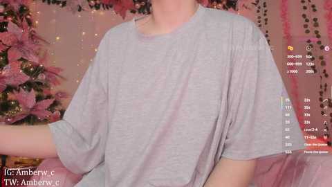 Video of a person in a gray T-shirt, seated in front of a pink, glittery Christmas tree, with a smartphone screen displaying a video recording and text overlay.