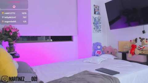 Video of a modern bedroom with purple lighting, plush toys, a large flat-screen TV, and a bed with white linens, framed by a pink wall.