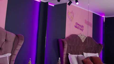 Video of a cozy, modern bedroom with a tufted, upholstered headboard, pink walls, purple accent lighting, and a mirror reflecting the bed.