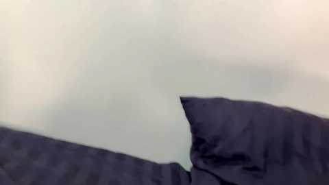 A video of a cat's head peeking out from under a dark blue blanket, its eyes partially visible. The background is blurred, suggesting a dim, indoor setting with soft lighting. The cat's fur appears short and sleek.