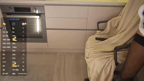 Video of a modern kitchen with beige cabinetry, a black chair draped in a beige blanket, and an oven on the left. A digital screen displays a cooking recipe with step-by-step instructions.