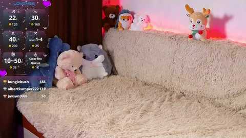 A cozy, warm video features plush toys on a soft, beige blanket in front of a Christmas tree. The background is a softly lit room with a wooden door.