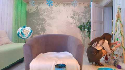 Video of a modern, pastel-themed bedroom with a girl painting a mural on the wall, a light gray armchair, a green bed, and a white floor lamp.