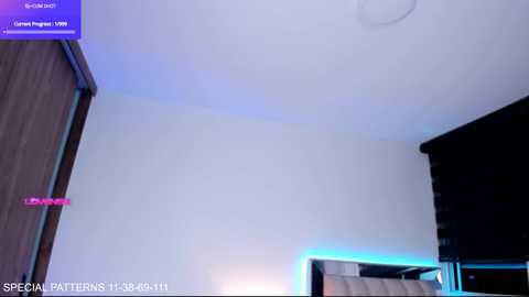 Video of a modern bedroom with a white ceiling, a dark dresser, a bed with a white headboard, and a blue light strip on the wall.