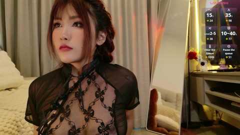 Video of an Asian woman with light skin and long brown hair in a black lace dress, gazing at a TV screen displaying a workout schedule.