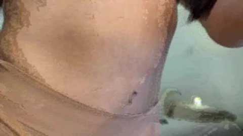 A close-up video of a wet, pale-skinned woman's torso in a bathtub, with water droplets and a lit candle in the blurred background.