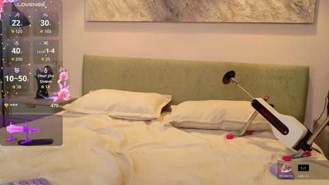 A video of a cozy, modern bedroom with a green upholstered headboard, two white pillows, a guitar, and a desk lamp on a bed. A large abstract painting hangs on the wall.