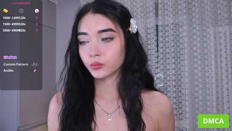 Media: Video of a young Asian woman with long black hair, wearing a floral hairpin, makeup, and a necklace, set against a silver backdrop.