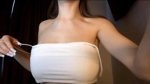 Media: Video of a woman with light skin and long brown hair, partially covered by a white towel, holding the towel's edge. Background features dark, possibly wooden, curtains.