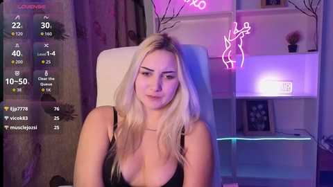 Video of a blonde woman in a black top, sitting in a white chair, with neon lights and digital stats overlay.