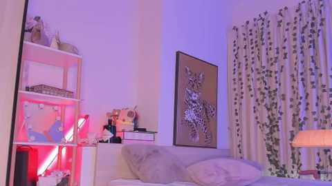 Media: Video of a modern, cozy bedroom with a bed, white walls, a beige lamp, a colorful abstract painting, and a decorative shelf with a neon light.