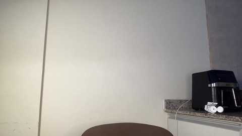 A video of a minimalist kitchen corner with a beige countertop, a black coffee maker, and white power cords, against a plain white wall.